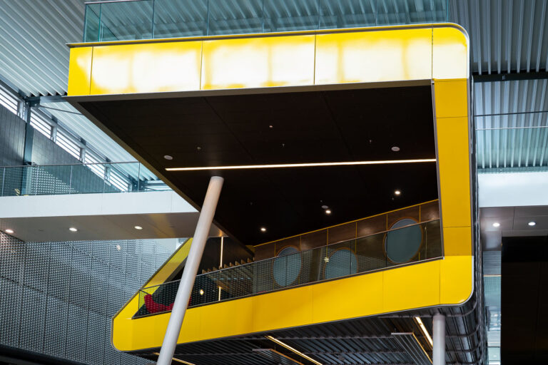 Modern Concourse Walkway, ExCeL London 3 A bold yellow cantilevered structure projects over the concourse at ExCeL London, the capital’s premier exhibition and convention complex in the Royal Docks. This elevated platform, supported by slanted steel columns and lined with circular observation windows, exemplifies the venue’s late-modern architectural style—combining industrial materials with contemporary design.
Part of the 2010s interior upgrades, the structure houses meeting and hospitality spaces overlooking the main exhibition halls below. Its polished metal, glass, and composite cladding echo the docklands’ engineering heritage while signaling ExCeL’s role as a centerpiece of London’s post-industrial regeneration and event economy.