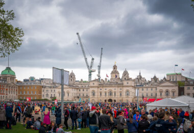 Participants and supporters gather at Horse Guards Parade near the finish area of the 2019 London Marathon. The scene captures the mix of exhaustion and celebration as runners cross the line against a backdrop of historic architecture and temporary infrastructure erected for the event. Cranes tower above the domes and facades of Whitehall’s government buildings, underscoring the juxtaposition of London’s centuries-old civic landmarks and its ever-changing skyline. The annual marathon, one of the world’s largest, draws tens of thousands of athletes and spectators to central London, filling the ceremonial grounds with color, energy, and determination.