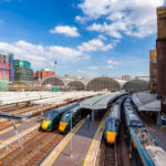 Modern high-speed trains wait beneath the soaring glass arches of Paddington Station in London, one of the capital’s busiest rail hubs. Designed in the mid-19th century by engineer Isambard Kingdom Brunel, the station blends historic architecture with the bustle of contemporary travel, serving as the terminus for Great Western Railway routes to Wales and the West Country. Around the concourse, new developments and construction highlight the area’s transformation, with Paddington’s mix of heritage and modernity on full display.