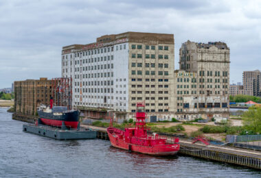 Once a centerpiece of London’s industrial age, Millennium Mills stands derelict on the south side of the Royal Victoria Dock in Silvertown. Built in 1905 for Spillers, the flour mill operated for decades before closing in the 1980s. The weathered façade and faded signage remain prominent features of the docklands skyline. Moored in front is the striking red Trinity House Lightship 93, formerly used as a floating lighthouse to warn ships at sea. Today, the area is part of the Royal Docks regeneration zone, blending remnants of Britain’s maritime and industrial heritage with modern redevelopment.
