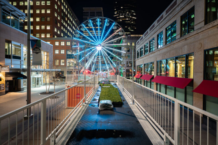 Night Lights on Nicollet During the Final Four 2 The bright blue Ferris wheel rises above Nicollet Mall in downtown Minneapolis, part of the city’s celebrations during the 2019 NCAA Final Four tournament. Set between modern office towers and historic facades, the installation turned the urban corridor into a festive promenade of color and motion. The glow from the wheel’s LEDs reflects off rain-dampened pavement and glass storefronts, capturing a rare moment when the city’s business district became an after-dark fairground alive with light, visitors, and late-spring energy.