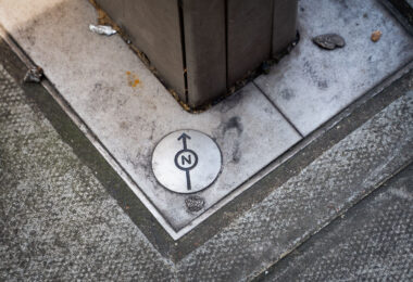 A small directional survey marker embedded in a London pavement, used by city planners and cartographers for geospatial alignment. The engraved north arrow and circular design mark an official reference point in the city’s street network, often tied to Ordnance Survey data and modern GIS mapping systems. These subtle fixtures are essential for maintaining urban infrastructure accuracy, helping surveyors and engineers align roadworks, utilities, and property boundaries with London’s broader coordinate grid.