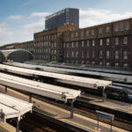 Paddington Station Platforms and the Historic GWR Train Shed 1 An elevated view of London Paddington Station shows the sweeping iron-and-glass train sheds designed in the mid-19th century for the Great Western Railway by Isambard Kingdom Brunel. The long canopies stretch over multiple platforms, where modern GWR Class 800 “Intercity Express” trains await departure. The adjacent red-brick offices of the original railway company still stand beside the terminus, a reminder of Paddington’s role as both a Victorian engineering triumph and a key link in Britain’s modern high-speed network.