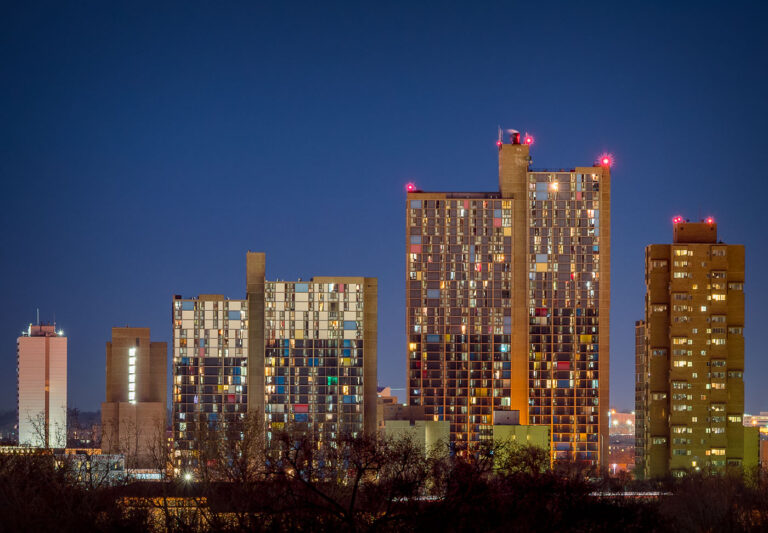 Riverside Plaza at Dusk 1 Riverside Plaza and Cedar High Apartments stand illuminated against the twilight sky in Minneapolis’ Cedar-Riverside neighborhood. Completed in the 1970s and designed by architect Ralph Rapson, the complex is one of the city’s most distinctive examples of modernist architecture. Its colorful paneling and Brutalist concrete forms house one of the most diverse communities in the region, symbolizing both urban renewal and the evolution of affordable housing in the Twin Cities.