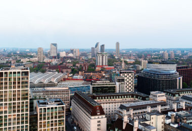 Captured from one of the observation capsules of the London Eye, this elevated southwest-facing view looks across the South Bank and Waterloo Station toward the district of Vauxhall and the emerging skyline of Nine Elms and Battersea. The large curved glass roofs of Waterloo Station dominate the foreground, marking one of London’s busiest rail terminals. Beyond it, a mix of modern residential towers—including St George’s Wharf Tower and various recent high-rise developments—signal the transformation of South London’s riverfront. The image illustrates the urban evolution from historic masonry buildings near the Thames to new commercial and residential architecture further out, highlighting London’s shifting development landscape.