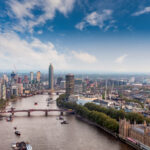 A sweeping view over central London captures the River Thames winding past Westminster toward the modern high-rises of Vauxhall and Nine Elms. On the right, the ornate Gothic Revival architecture of the Palace of Westminster anchors the historical core of the city, while Lambeth Bridge spans the river ahead. Across the Thames, cranes and towers mark London’s expanding skyline, where new residential and commercial developments rise along the South Bank. The image reflects both the enduring legacy of Victorian engineering and the ongoing transformation of London’s riverfront into a dense corridor of 21st-century architecture.
