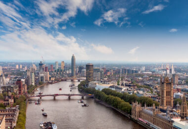 A sweeping view over central London captures the River Thames winding past Westminster toward the modern high-rises of Vauxhall and Nine Elms. On the right, the ornate Gothic Revival architecture of the Palace of Westminster anchors the historical core of the city, while Lambeth Bridge spans the river ahead. Across the Thames, cranes and towers mark London’s expanding skyline, where new residential and commercial developments rise along the South Bank. The image reflects both the enduring legacy of Victorian engineering and the ongoing transformation of London’s riverfront into a dense corridor of 21st-century architecture.