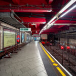 Baker Street Station’s Metropolitan Line platforms represent one of the oldest sections of the London Underground, opened in 1863 as part of the world’s first subterranean railway. The terminus platforms, seen here, retain their cut-and-cover Victorian brickwork paired with modern safety updates and striking red-painted steel reinforcements added during later refurbishments.

The station originally served the Metropolitan Railway’s steam-hauled trains running between Paddington and Farringdon before electrification in the early 20th century transformed the network. Period signage advertising “Chiltern Court” and the original Metropolitan Railway branding pay homage to its heritage, contrasting with the exposed wiring, signal lights, and tiling that reveal more than 160 years of evolving underground infrastructure. Today, Baker Street remains a key interchange, connecting five Underground lines while preserving much of the industrial atmosphere that defined London’s pioneering approach to mass transit.
