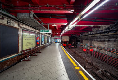 Baker Street Station’s Metropolitan Line platforms represent one of the oldest sections of the London Underground, opened in 1863 as part of the world’s first subterranean railway. The terminus platforms, seen here, retain their cut-and-cover Victorian brickwork paired with modern safety updates and striking red-painted steel reinforcements added during later refurbishments.

The station originally served the Metropolitan Railway’s steam-hauled trains running between Paddington and Farringdon before electrification in the early 20th century transformed the network. Period signage advertising “Chiltern Court” and the original Metropolitan Railway branding pay homage to its heritage, contrasting with the exposed wiring, signal lights, and tiling that reveal more than 160 years of evolving underground infrastructure. Today, Baker Street remains a key interchange, connecting five Underground lines while preserving much of the industrial atmosphere that defined London’s pioneering approach to mass transit.