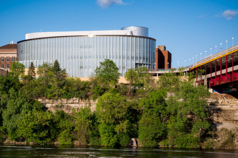 University of Minnesota’s Bruininks Hall Above the Mississippi 1 Bruininks Hall, with its curved glass facade and modernist profile, stands prominently on the bluffs of the Mississippi River at the University of Minnesota’s East Bank campus. The building, named after former university president Robert Bruininks, houses student services and administrative offices while serving as a visual landmark along the riverfront. The structure’s sleek transparency contrasts with the limestone layers of the bluff below, emphasizing the union between natural geology and contemporary academic architecture that defines much of the university’s riverfront setting.