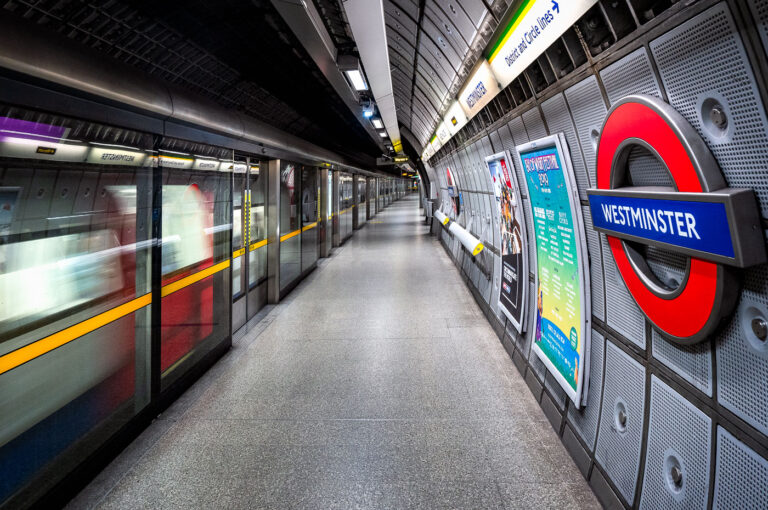 Westminster Underground Station – Jubilee Line Platform 2 The Jubilee Line platforms at Westminster Underground Station represent the deep-level engineering and modernist design of London’s late-20th-century transit expansion. Constructed as part of the 1999 Jubilee Line Extension, these platforms sit approximately 30 meters below ground, directly beneath the District and Circle line tunnels. Designed by Foster + Partners, the station features full-height platform screen doors — a safety innovation uncommon on most of the Underground — and a sleek system of acoustic panels and perforated aluminum cladding that enhance both sound control and visual uniformity.Every structural and material detail reflects the project’s dual purpose: to manage immense passenger flow serving Parliament and Whitehall above, while preserving architectural clarity within a highly constrained urban site. The smooth curvature of the platform walls, precision lighting, and isolation of mechanical systems behind layered steel panels highlight the station’s integration of industrial functionality with the aesthetics of modern infrastructure.