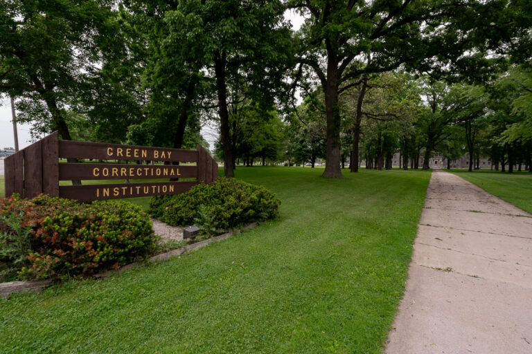 Entrance to Green Bay Correctional Institution, Allouez, Wiscons 1 The entrance to Green Bay Correctional Institution in Allouez, Wisconsin, shows the tree-lined approach to one of the state’s oldest operating prisons. Opened in 1898 as the Wisconsin State Reformatory, the facility was designed during an era emphasizing reform and rehabilitation, reflected in its spacious campus and classical stone buildings visible in the distance. Today, the institution remains part of the Wisconsin Department of Corrections system, standing as a significant piece of the state’s correctional history and architectural heritage.