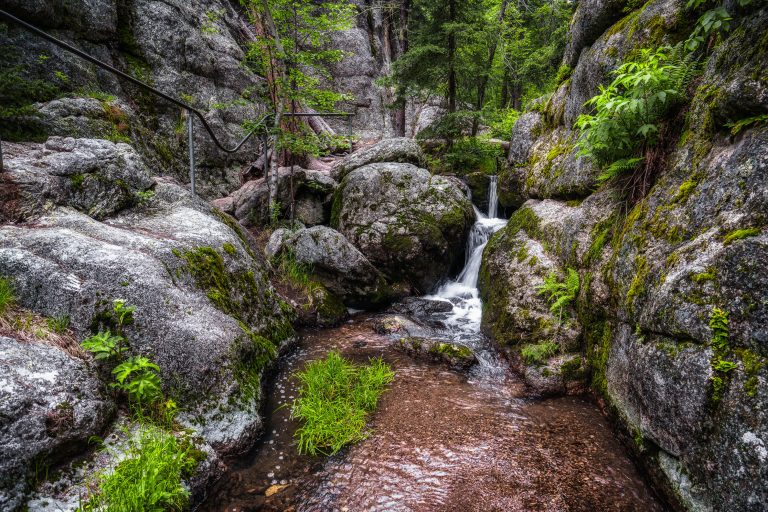 Granite Boulder Cascade Near Sylvan Lake, Custer State Park 1 A small waterfall flows through moss-covered granite boulders in a forested canyon at Sylvan Lake, South Dakota.