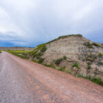 Sheep Mountain, Badlands National Park 2 A weathered wooden sign marks the rugged entrance to Sheep Mountain in the southern reaches of Badlands National Park, South Dakota. This remote area, surrounded by the sweeping prairies of Buffalo Gap National Grassland, offers one of the park’s most dramatic and less-visited overlooks. The region sits within Oglala Lakota lands, where erosion has sculpted colorful buttes and steep ridges over millions of years. Accessible by an unpaved road, Sheep Mountain remains a quiet, untamed corner of the Badlands, revealing the deep geologic and cultural layers of the Northern Plains.