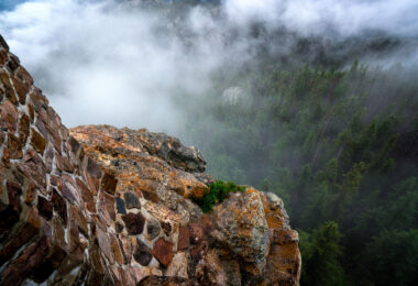 At the summit of Black Elk Peak, low clouds roll through the granite spires and dense pine forest below, wrapping the mountain in a shifting veil of fog. The historic stone fire tower, built by the Civilian Conservation Corps in the 1930s, stands as a testament to early forest conservation in the Black Hills. From this vantage point—the highest in South Dakota—views often stretch into Wyoming and Nebraska, but on misty mornings like this one, the world feels confined to the mountaintop itself, suspended between rock and cloud.