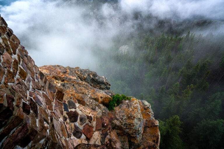 Summit Fog on Black Elk Peak 3 At the summit of Black Elk Peak, low clouds roll through the granite spires and dense pine forest below, wrapping the mountain in a shifting veil of fog. The historic stone fire tower, built by the Civilian Conservation Corps in the 1930s, stands as a testament to early forest conservation in the Black Hills. From this vantage point—the highest in South Dakota—views often stretch into Wyoming and Nebraska, but on misty mornings like this one, the world feels confined to the mountaintop itself, suspended between rock and cloud.