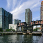 The iconic Long Island sign towers over the East River waterfront in Queens as evening light reflects off the glassy high-rises of Long Island City. Once a gritty industrial dock, the area has transformed into one of New York City’s fastest-growing neighborhoods.