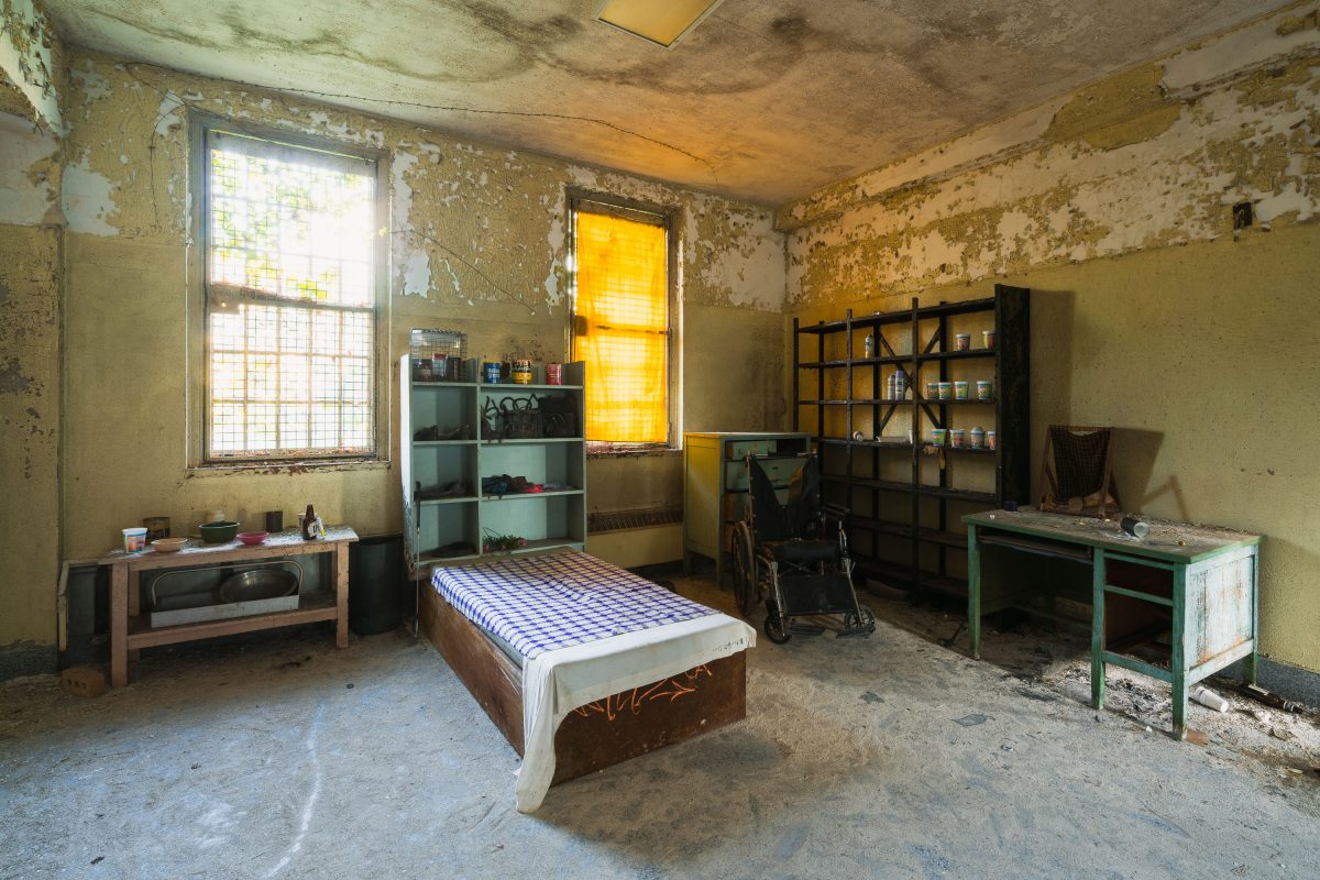 Deteriorated bedroom at abandoned Creedmore Psychiatric Center in Queens, New York, with peeling walls and institutional
