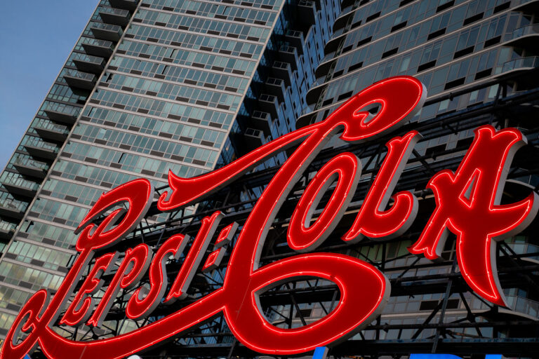 Pepsi-Cola Sign Long Island City 3 The iconic Pepsi-Cola sign glows in red neon along the East River waterfront in Long Island City, Queens. The landmark sign, originally installed in 1936, now stands in front of modern residential towers and remains a prominent feature of the New York City skyline.
