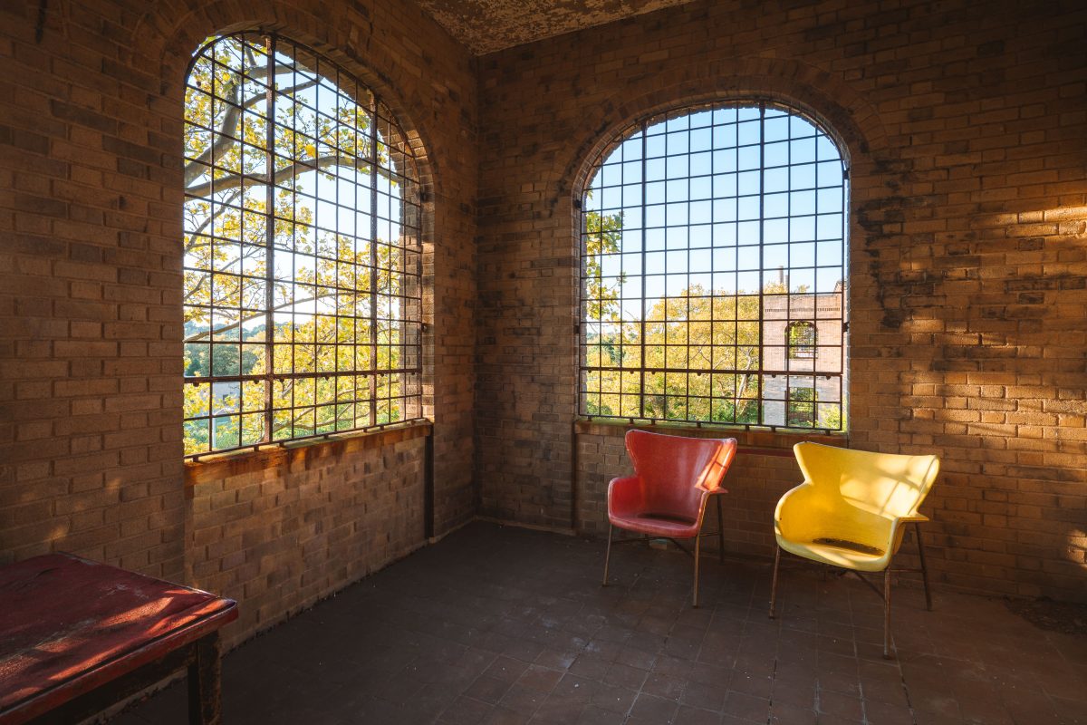 Red and yellow chairs in a brick room at Creedmore Psychiatric Center, New York, viewed through barred windows.