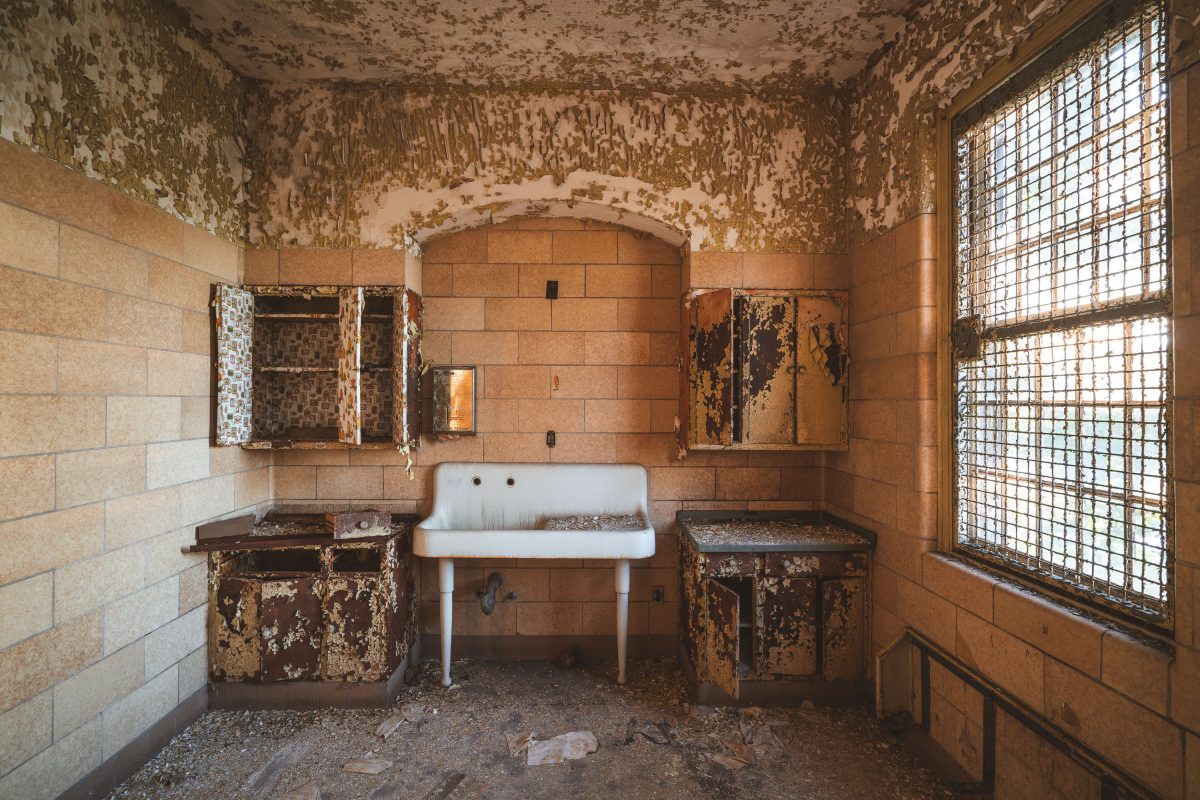 Deteriorated bathroom with rusted fixtures and peeling walls at abandoned Creedmore Psychiatric Center in Queens, New York.