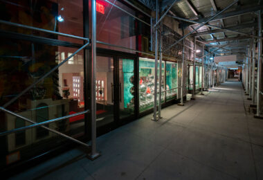 Sidewalk on Madison Avenue showing a row of storefronts under scaffolding late at night on Madison Avenue in Manhattan. The Christian Louboutin store window.