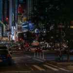 Traffic and illuminated billboards fill Times Square in Manhattan at night, with streams of cars and taxis moving through the crowded intersection. Bright advertisements, theater signs, and neon lights dominate the scene as pedestrians navigate the sidewalks and bike lanes around one of New York City’s busiest landmarks.