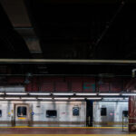 A Metro-North Railroad train sits at a platform inside Grand Central Terminal in Manhattan. The stainless-steel cars reflect the dim lighting of the underground station, where exposed pipes and graffiti-marked beams highlight the aging infrastructure of the busy commuter hub.