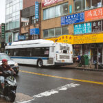 An MTA bus is stopped along Roosevelt Avenue in Flushing, Queens, a bustling corridor lined with Chinese and Korean storefronts.