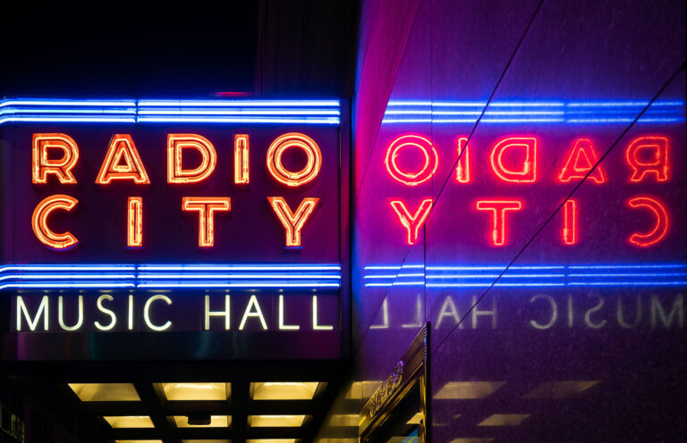 Radio City Music Hall Neon Sign, New York City 1 The neon sign for Radio City Music Hall in New York City illuminates the building at night.