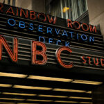 The neon marquee of NBC Studios glows outside 30 Rockefeller Plaza in Midtown Manhattan. The sign, also advertising the Rainbow Room and the building’s observation deck, marks the entrance to the historic headquarters of the television network.