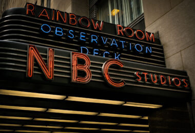 The neon marquee of NBC Studios glows outside 30 Rockefeller Plaza in Midtown Manhattan. The sign, also advertising the Rainbow Room and the building’s observation deck, marks the entrance to the historic headquarters of the television network.