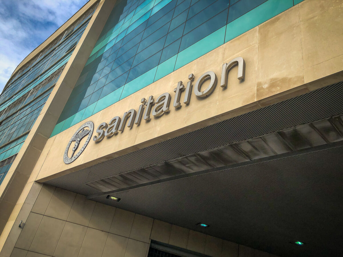 The New York City Department of Sanitation Headquarters building features prominent signage and the department's seal on a facade of stone tiles and glass.