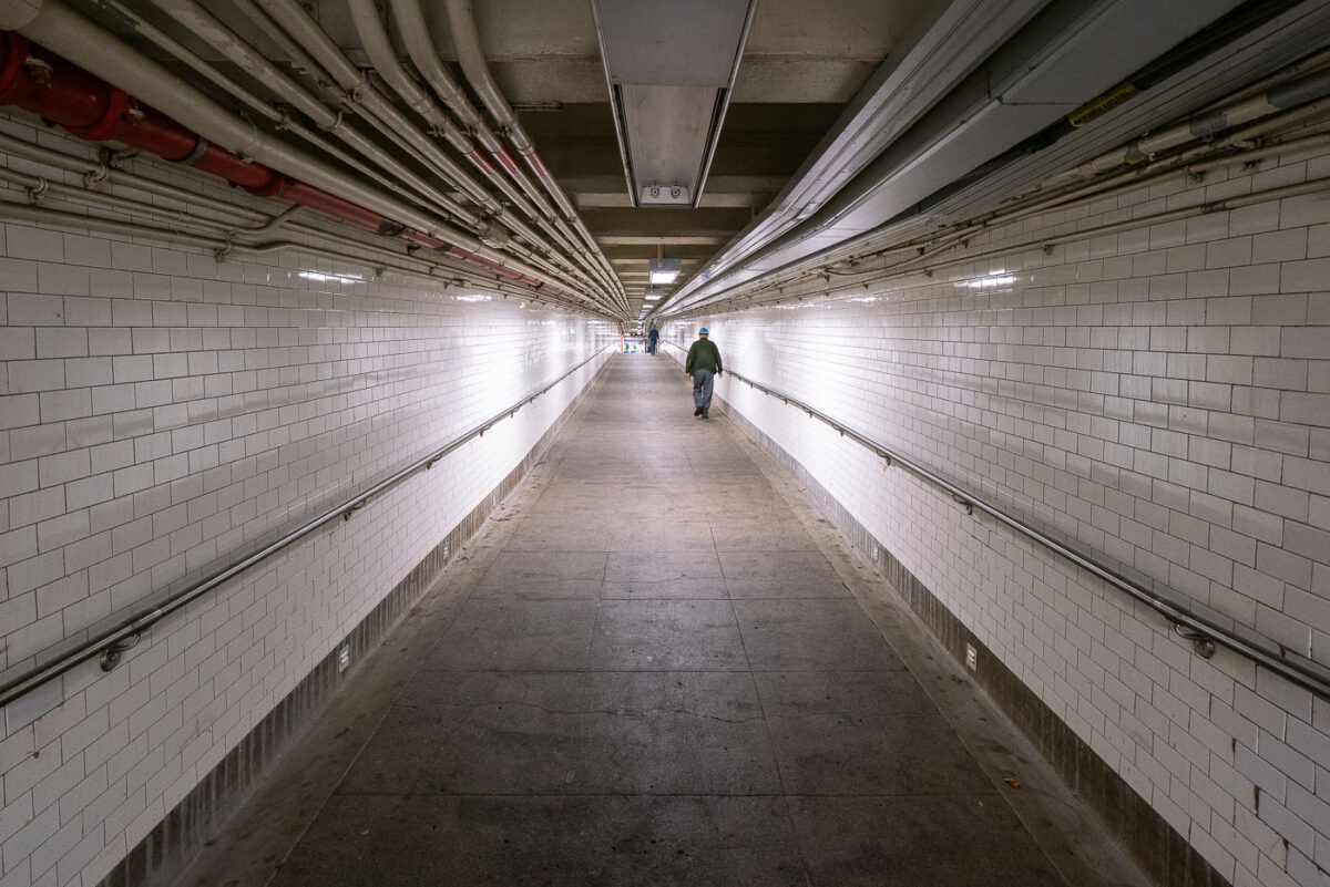 A man walks down a long hallway in the New York City Subway system.