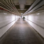 A man walks down a long hallway in the New York City Subway system.