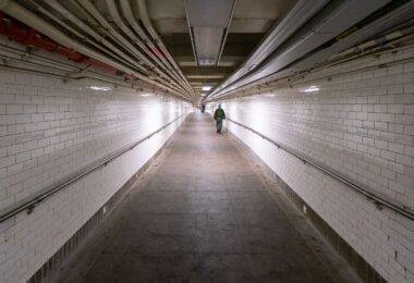 A man walks down a long hallway in the New York City Subway system.