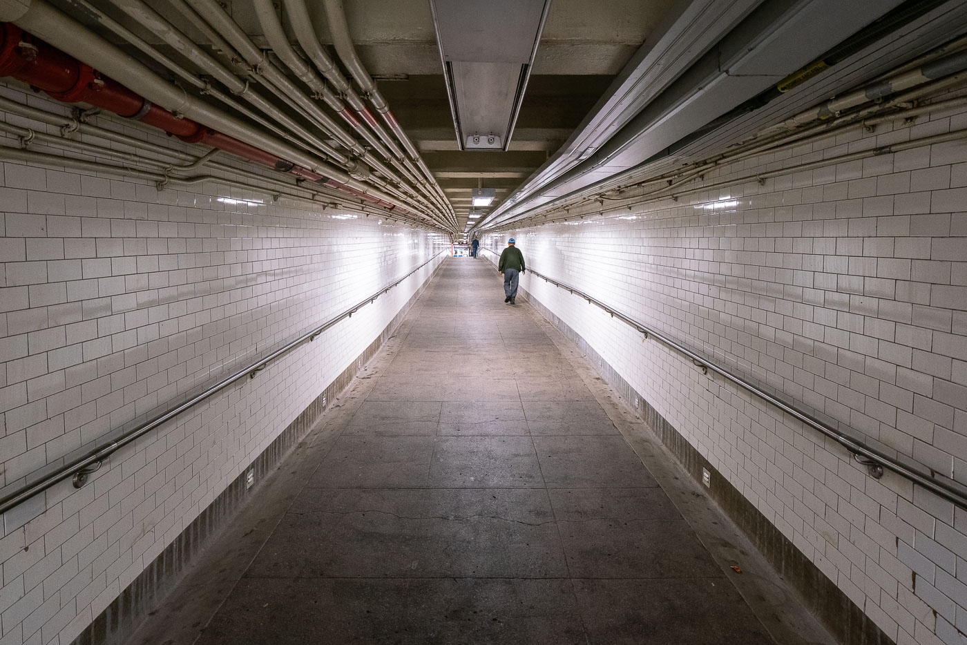 A man walks down a long hallway in the New York City Subway system.