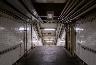 A dimly lit stairway leads down into a New York City subway station on Sunday, Sept. 14, 2025. Aging infrastructure and exposed piping are visible along the tiled walls.