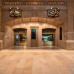 The entrance to Track 30 inside Grand Central Terminal in Manhattan is seen at night. The marble hallways of the landmark station lead to the train platforms below, as a commuter and a security officer stand near the archways beneath illuminated signs.