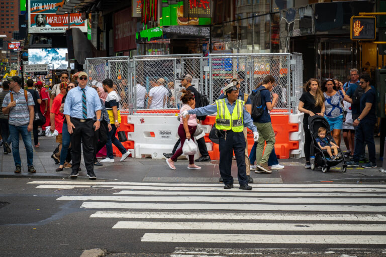 NYPD Traffic Police 3 A traffic officer directs pedestrians at a crosswalk in Times Square, Manhattan. Crowds move past construction barriers and street signage in the busy tourist district, where theaters, billboards, and entertainment venues draw thousands of visitors daily.