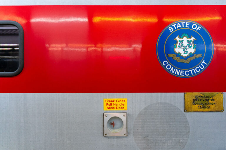 State of Connecticut seal on a train 3 A Connecticut state seal is displayed on the side of a Metro-North Railroad train car, operated in partnership with the Connecticut Department of Transportation. The red-and-silver exterior includes safety instructions and signage, highlighting the regional rail system that connects commuters between New York and Connecticut.