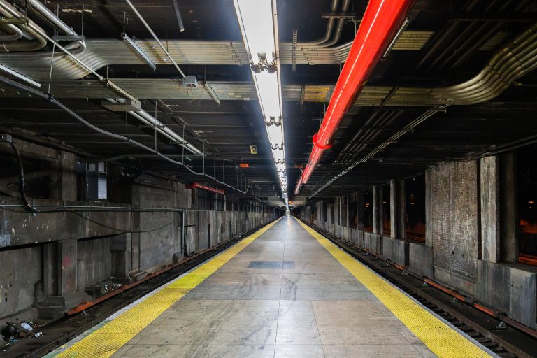 Empty subway platform at Grand Central Terminal with yellow safety line and red overhead lighting.