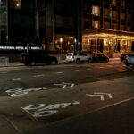 The entrance of Trump International Hotel and Tower in Manhattan is seen at night. Several vehicles, including an NYPD patrol car, are parked outside the building along a marked bike lane.