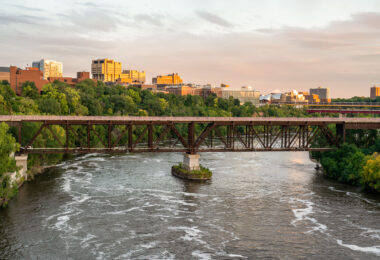 Bridges linking the University of Minnesota East and West banks in Minneapolis. Evening light reflects off campus buildings, including the Weisman Art Museum and the Phillips-Wangensteen Building.