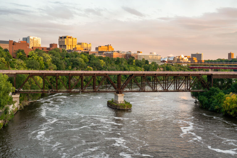 University of Minnesota Bridges Over The Mississippi River 2 Bridges linking the University of Minnesota East and West banks in Minneapolis. Evening light reflects off campus buildings, including the Weisman Art Museum and the Phillips-Wangensteen Building.