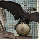 An eagle statue perched on a globe stands outside Grand Central Terminal in Manhattan. The bronze sculpture, one of several around the historic landmark, looks out over Midtown with the glass facade of the MetLife Building rising in the background.