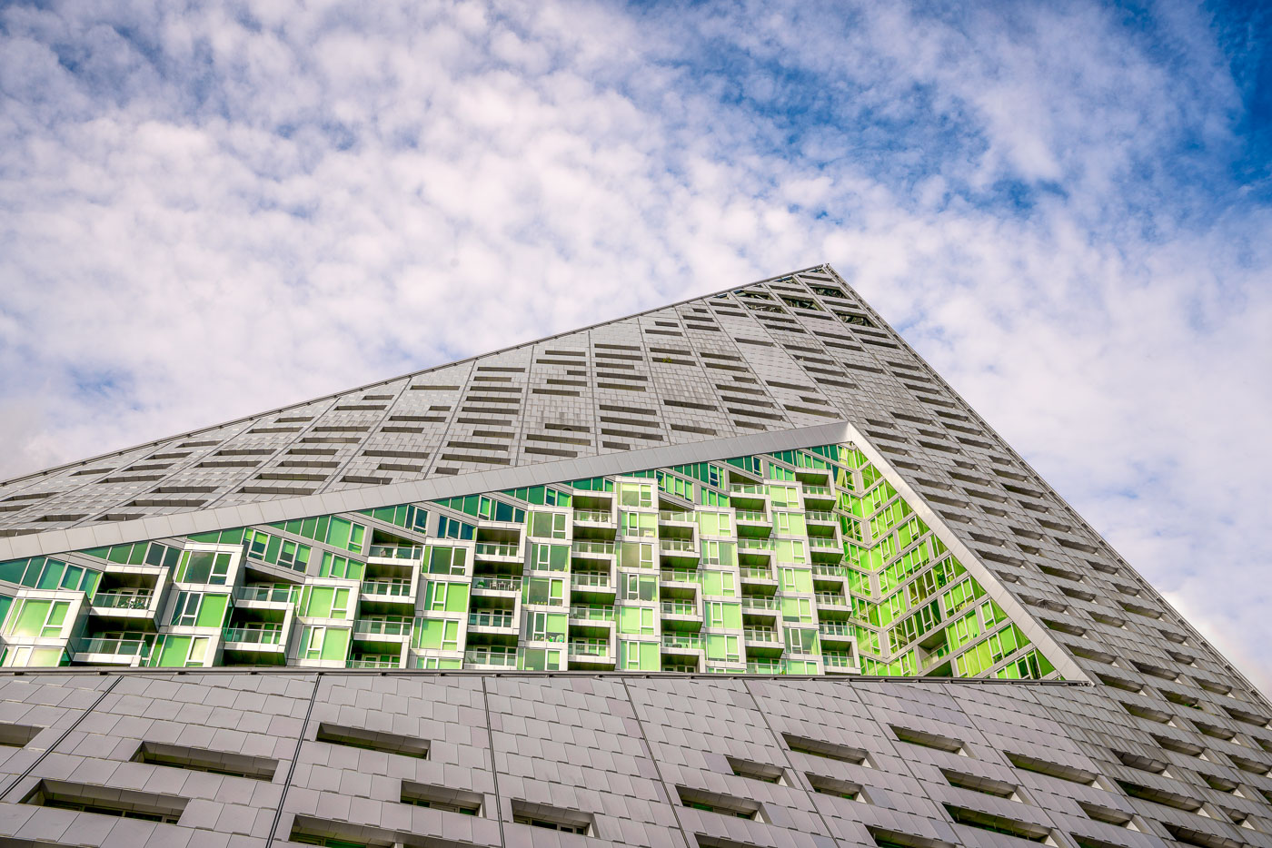 The VIA 57 West residential building in New York City, designed by Bjarke Ingels Group, features a distinctive pyramidal form with a grey facade and green-tinted glass balconies.