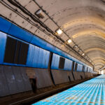 The curved platform of a Chicago Transit Authority Blue Line station reveals the utilitarian design of the city’s subway infrastructure, part of the Milwaukee–Dearborn subway opened in 1951. The tunnel’s tiled blue panels and low arched ceiling reflect the postwar engineering era that brought rapid transit beneath the Loop and the West Side, connecting O’Hare International Airport to downtown. Despite its age, this corridor remains a vital artery in Chicago’s daily commuter network, a symbol of mid-century urban mobility still in constant motion beneath the city streets.