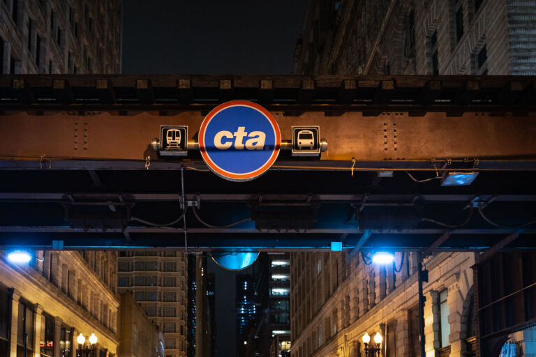 Chicago ‘L’ Structure and CTA Sign in the Loop 2 The Chicago Transit Authority (CTA) logo is displayed beneath the steel elevated tracks that define the Loop, the city’s central business district. The structure, part of the “L” system first built in the late 19th century, remains one of Chicago’s most enduring symbols of urban mobility. Overhead girders and riveted beams—many still original to the early 1900s—carry trains above streets lined with early skyscrapers and historic facades. The CTA continues to operate one of the largest and oldest public transit networks in the United States, moving more than a million riders daily through Chicago’s interconnected system of rail and bus lines.