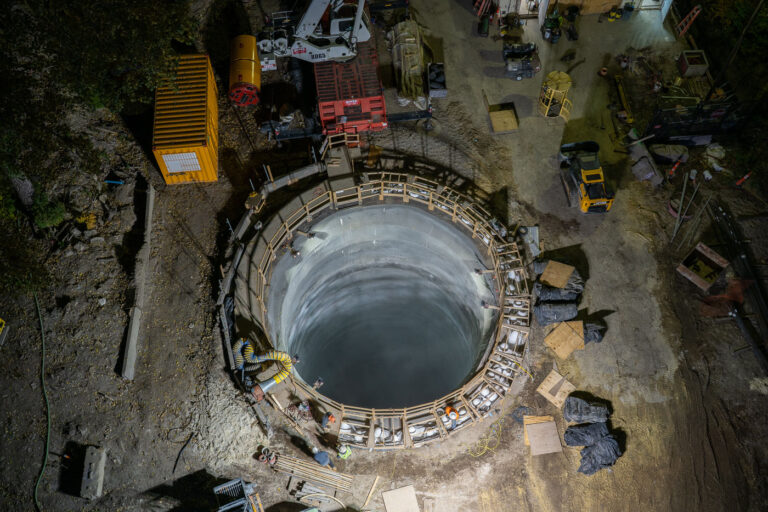 Deep Shaft Construction for Mississippi River Tunnel 4 An aerial view captures the excavation shaft for a massive water main tunnel beneath the Mississippi River. The reinforced concrete cylinder serves as the launch point for a tunnel boring machine, visible nearby, which will cut through layers of limestone and shale to create a new conduit linking the city’s water systems. The project represents a critical upgrade to regional infrastructure, designed to improve reliability and resilience while accommodating future demand across Minneapolis and St. Paul.